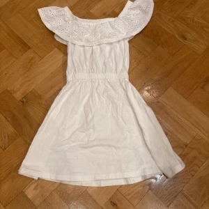 Vit klänning från Primark - Söt vit klänning från Primark med en vacker spetsdetalj runt halsen. Klänningen har en elastisk midja och är perfekt för somriga dagar. Den är axelbandslös och har en luftig passform. Perfekt för en liten fashionista! 🌸