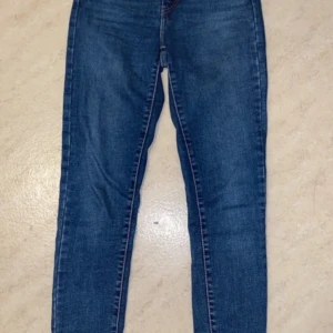 Blå jeans från Levi's - Blå jeans från Levi's med klassisk femficksdesign och knappgylf. De har en smal passform.