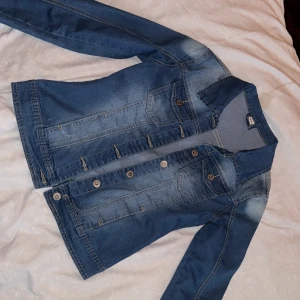 Blå jeansjacka - Säljer en klassisk blå jeansjacka med knappar framtill. Jackan har långa ärmar och två bröstfickor med knappstängning. Perfekt för en avslappnad stil.  Använd 1 gång.