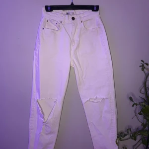 Vita jeans med slitningar - Snygga vita jeans med slitningar på knäna. De har en klassisk femficksdesign och knäppning fram. Perfekta för en avslappnad stil. Midrise och sitter super fint i midjan.
