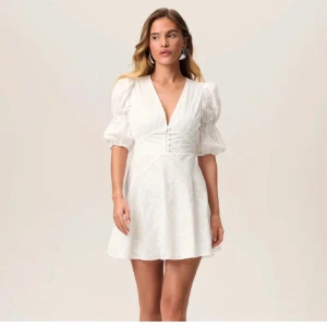 Vit kortklänning med puffärmar från Adoore - Säljer en söt vit kortklänning med puffiga kortärmar och v-ringning. Klänningen har knappar framtill och ett fint blommigt mönster. Perfekt för studenten! Endast testat. Köpt på Sellpy för 1500 i originala förpackningen