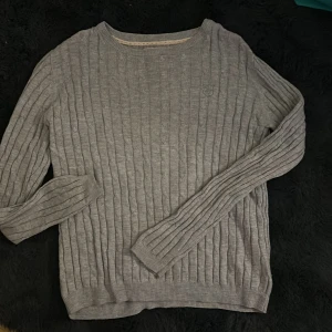 Grå stickad tröja från Hampton Republic - Säljer en stilren grå stickad tröja från Hampton Republic. Tröjan har ett diskret mönster och en broderad logga på framsidan. Perfekt för kyligare dagar med sin mjuka och bekväma passform. Passar både till vardags och mer uppklädda tillfällen.