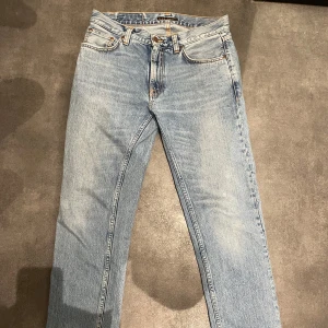 Ljusblå jeans från Nudie Jeans - Snygga ljusblå jeans från Nudie Jeans med klassisk femficksdesign och orange sömmar. De har en normal passform och är tillverkade i slitstarkt denim. Perfekta för en avslappnad stil. Modell Gritty Jackson.