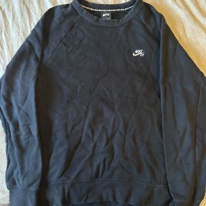 Svart sweatshirt från Nike SB - Säljer en stilren svart sweatshirt från Nike SB med deras logga broderad på bröstet. Tröjan har långa ärmar och en rund halsringning. Litet hål i ryggen.