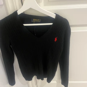 Svart tröja från Ralph Lauren - Snygg svart tröja från Ralph Lauren med v-ringning och det klassiska röda logotypbroderiet på bröstet. Tröjan har långa ärmar och är perfekt för en stilren look.