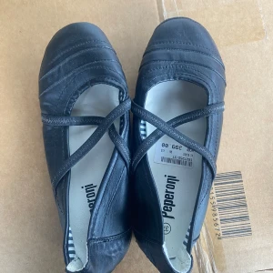 Svarta ballerinaskor från Peperoni - Snygga svarta ballerinaskor från Peperoni med korsade remmar över foten. Perfekta för en stilren look. Skorna har en rund tå och är tillverkade i ett material som ger en elegant finish.