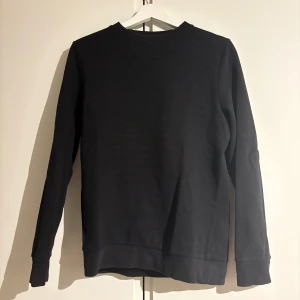 Svart långärmad tröja - (StorlekXS/S) Säljer en stilren svart långärmad tröja med rund hals. Perfekt för en enkel och avslappnad look. Tröjan har en diskret ribbad struktur som ger den lite extra karaktär.