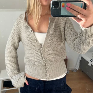 Beige stickad kofta - Säljer en mysig beige stickad kofta med knappar framtill. Koftan har långa ärmar och en klassisk design som passar perfekt för kyligare dagar. Perfekt att ha över en topp eller klänning för extra värme.