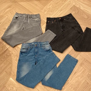 Tre par jeans från LAB Industries - Säljer tre par jeans från LAB Industries. Ett par är ljusblå med klassisk femficksdesign, ett par är grå med snörning i midjan, och det sista paret är svart med knappstängning. Perfekta för olika tillfällen och stilar.