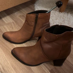 Bruna boots med dragkedja - Snygga bruna boots i skinn med dragkedja på sidan och en bekväm klack. Perfekta för höst och vår, dessa boots har en spetsig tå som ger en elegant touch.