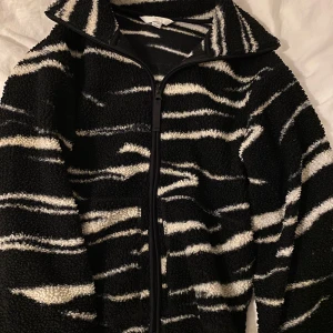 Zebra fleece från hm - Säljer en mysig svart och vit fleecejacka med zebramönster. Jackan har en dragkedja framtill och långa ärmar. Perfekt för kyliga dagar när du vill vara både varm och stilren. 🖤🤍