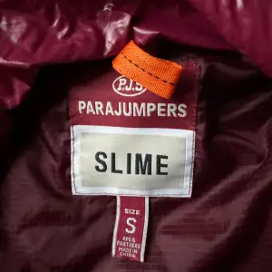 Säljer en snygg vinröd dunjacka från Parajumpers. Jackan har en quiltad design med dragkedja och en hög krage. Perfekt för kyliga dagar och ger en stilren look. Märkeslogga på ärmen ger en extra touch.