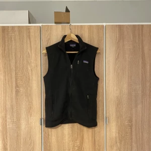 Svart fleeceväst från Patagonia - Säljer en svart/ mörkgrå fleeceväst från Patagonia med dragkedja framtill och två praktiska fickor. Perfekt för lager-på-lager under kyliga dagar. Västen har en klassisk design och är både stilren och funktionell. Kan även bytas mot en likadan i en större storlek