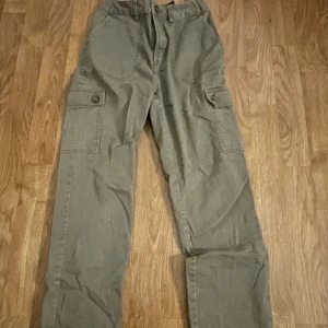Gröna cargobyxor - Snygga gröna cargobyxor med flera praktiska fickor och knappdetaljer. Perfekta för en avslappnad stil med en loose passform. Byxorna har en klassisk design med raka ben och är tillverkade i ett slitstarkt material.