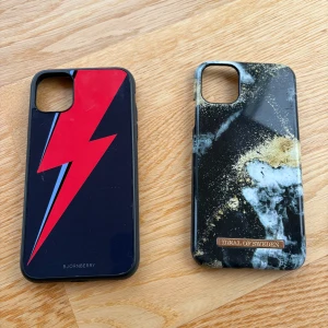 Två mobilskal från Bjornberry och iDeal of Sweden - Säljer två snygga iPhone 11 mobilskal. Ett från Bjornberry med en röd blixt på svart bakgrund och ett från iDeal of Sweden med ett marmorerat mönster i svart, vitt och guld. Perfekt för att ge din mobil en ursnygg still. Har mögra defekter men inget man tänker på❤️💕