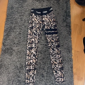 Leopardmönstrade träningsbyxor från Stronger - Leopardmönstrade träningsbyxor från Stronger med hög midja och elastisk linning. Perfekta för träning eller en trendig vardagslook. Materialet är stretchigt och bekvämt. Priset kan diskuteras.