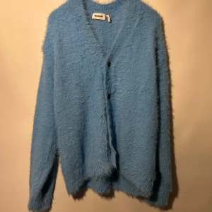 Blå fluffig kofta från Weekday - Ljusblå, fluffig kofta med V-ringning och knappar framtill. Koftan har en avslappnad passform och långa ärmar. Mycket bra skick, sparsamt använd