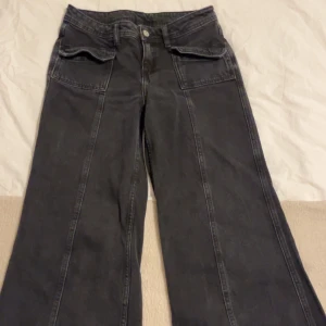 Svarta jeansbyxor med vida ben - Snygga svarta jeansbyxor med vida ben och framträdande sömmar. Byxorna har fickor både fram och bak samt en klassisk dragkedja och knapp framtill. Perfekta för en avslappnad stil. Köpta från beyond retro  70tals flare! 
