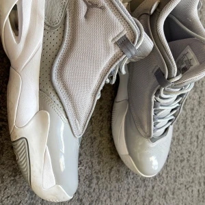 Grå sneakers från Nike - Snygga grå sneakers från Nike med en stilren design. Skorna har snörning och en kombination av olika grå nyanser i både syntet och skinnmaterial. Perfekta för en sportig look.