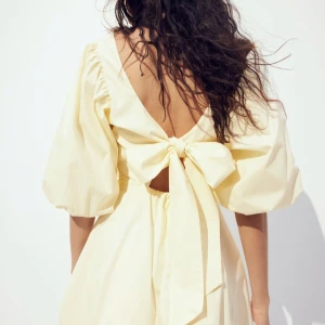 Ljusgul klänning med puffärmar - Charmig ljusgul klänning med puffiga trekvartsärmar och en stor rosett i ryggen. Från H&M och är aldrig använd!!