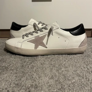 Golden goose  - Snygga sneakers av märket golden goose, med en grå stjärna på sidan och grå snörning. Skorna har en svart häl och en robust sula. Perfekta för våren/sommaren och överlag ett par jävligt goa skor. De sitter hyfsat litet i storleken och passar nog även 45. Det medföljer box som är lite skadad men inget man behöver oroa sig över, det tillkommer tyvärr inte andra saker som orginal påse mm. Därav priset:).