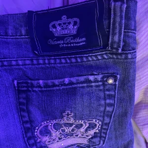 Jeans från Victoria Beckham - Snygga jeans från Victoria Beckham med en cool broderad krona på bakfickan. De har en klassisk blå färg och en straight passform. Tyvärr är dom lite slitna längst ner.