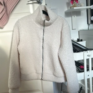 Vit teddyjacka från Zink - Mysig vit teddyjacka från Zink i storlek S. Jackan har en dragkedja framtill och är långärmad med en hög krage. Perfekt för kyliga dagar när du vill hålla dig varm och bekväm.
