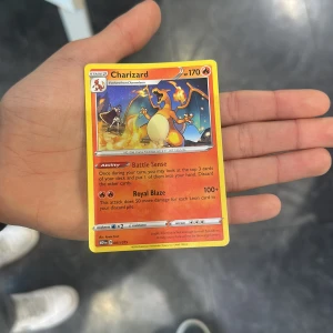 Charizard Pokémon-kort - Säljer ett Charizard Pokémon-kort med 170 HP. Kortet har förmågan 'Battle Sense' och attacken 'Royal Blaze'. Perfekt för samlare eller spelare som vill stärka sin kortlek. Kortet har en ikonisk design med Charizard i en kraftfull pose.