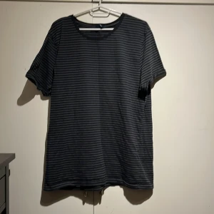 Svart och grå randig t-shirt från Iconic Sport 157 - Säljer en svart och grå randig t-shirt från Iconic Sport. Den har en avslappnad passform och korta ärmar, perfekt för en casual look. T-shirten är tillverkad i ett mjukt material som känns skönt mot huden.