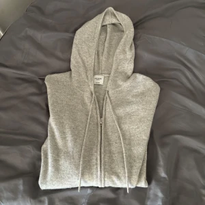 Grå cashmere hoodie från John Henric - Säljer en lyxig grå hoodie i 100% cashmere från John Henric. Den har en dragkedja framtill och en justerbar huva med snören. Perfekt för en stilren och bekväm look. 🧥✨