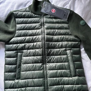 Colmar Cardigan  - Snygg grön jacka från Colmar med quiltad design och stickade ärmar. Jackan är även helt ny med prislapp. Jackan har en dragkedja framtill och två fickor med dragkedja. Perfekt för kyligare dagar med sin stilrena look och bekväma passform. 