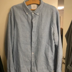 Ljusblå skjorta från Elvine - Säljer en stilren ljusblå skjorta från Elvine. Skjortan har långa ärmar och knappar framtill. Perfekt för en avslappnad men ändå uppklädd look. Passar bra till både jeans och chinos.