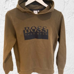 Hugo Boss - Säljer en snygg olivgrön hoodie från Hugo Boss med deras ikoniska logga tryckt på framsidan. Perfekt för en avslappnad stil. Hoodien har långa ärmar och en klassisk huva.