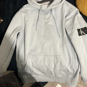 Ljusblå hoodie från Calvin Klein Jeans - Säljer en stilren ljusblå hoodie från Calvin Klein Jeans. Tröjan har en klassisk design med dragsko i huvan och en ficka framtill. Perfekt för en avslappnad look.