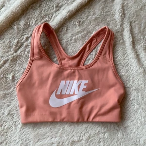 Rosa sporttopp från Nike - Säljer en snygg rosa sporttopp från Nike med vit logga framtill. Toppen har en racerback-design och är tillverkad i ett mjukt och stretchigt material för optimal komfort under träning.