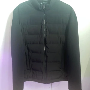 Svart jacka från Zara - Säljer en stilren svart jacka från Zara. Jackan har en dragkedja framtill och är långärmad. Perfekt för kyligare dagar med sin quiltade design. Använt en gång.
