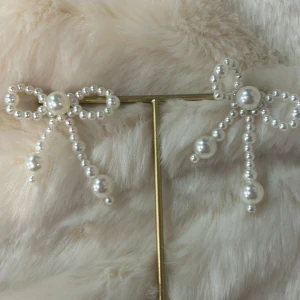 Vita pärlörhängen med rosett - Charmiga örhängen formade som rosetter, dekorerade med vita pärlor. Perfekta för att ge en elegant touch till din outfit. De hänger fint och har en unik design som drar blickarna till sig.