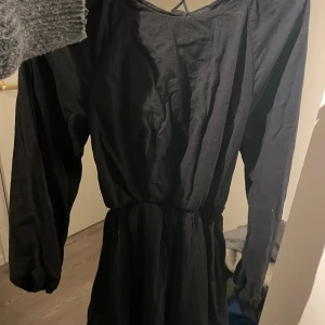 Svart klänning med lång ärm - Snygg svart klänning med långa ärmar och en elegant passform. Klänningen har en knytning i ryggen som ger en fin detalj. Perfekt för en stilren look.