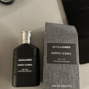 Simply Iconic Eau de Toilette från Jack & Jones - Säljer en elegant Eau de Toilette från Jack & Jones, Simply Iconic. Flaskan är svart med en stilren design och har en silverfärgad kork. Förpackningen är grå med ett textilmönster. Perfekt för den som söker en tidlös doft.