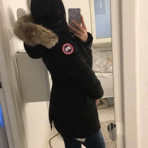 Svart canada goose parkajacka  - Säljer en  Canada Goose med pälsdetalj luvan. Jackan har en klassisk design med lång ärm och är perfekt för kalla dagar. Den har en snygg passform och är både stilren och funktionell. Har inget kvitto kvar då jag köpte den för flera år sedan. Lite trasig på under armen men går att fixa hos sömmerska tror jag. Två knappar baktill är av.  där av billigare precis går snabbt ner i pris med tanke på trasig vid armen. Nypris 10.500. Är en XXS men passar xs/s med. Du står för frakten. 