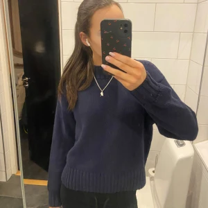 Mörkblå stickad tröja från Gina Tricot - Säljer en stilren mörkblå stickad tröja från Gina Tricot. Tröjan har en klassisk rund halsringning och långa ärmar med ribbade muddar. Perfekt för kyligare dagar. Passar till både jeans och kjol.