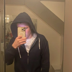 Mörkblå huvtröja från Ralph Lauren - Säljer en snygg mörkblå huvtröja från Ralph Lauren med dragkedja och vit dragsko. Den har en röd broderad logotyp på bröstet och är perfekt för en avslappnad stil. Passar bra till både jeans och träningsbyxor.