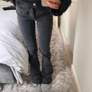 Svarta jeans med dragkedjedetaljer - Snygga svarta jeans med bootcut och dragkedjor vid fickorna. De är lågmidjade och har en svart/grå tvätt. Jeansen har en rak stil och är tillverkade i ett bekvämt material.