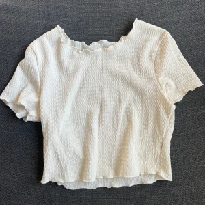  ribbad topp - Säljer en söt ribbad topp med korta ärmar och vågig kant. Perfekt för sommardagar eller som ett basplagg i garderoben. Toppen har en mjuk och stretchig känsla, vilket gör den bekväm att bära hela dagen.