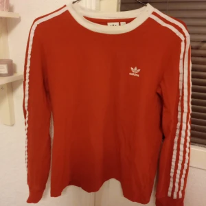 Röd långärmad tröja från Adidas - Säljer en långärmad adidas tröja i strl M, den är mörkare röd än vad den är på bilderna! Enstaka fläckar kolla två sista bilderna, det går nog bort i tvätten, tröjan är sliten! Bra skick! Säljer den för 50kr + frakt!