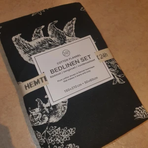 Bäddset - Säljer ett mysigt svart bäddset i bomullsflanell från Hemtex. Setet har ett vackert vitt mönster med djur och löv. Storleken är 150x210 cm för påslakanet och 50x60 cm för örngottet. Perfekt för att hålla sig varm och bekväm under kalla nätter. 🍂