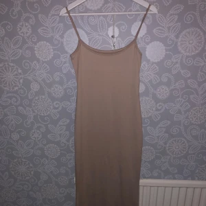 Beige axelbands klänning - Säljer en stilren beige klänning med smala axelband. Perfekt för sommardagar eller som en bas i garderoben. Klänningen har en enkel och elegant design som passar till många tillfällen.