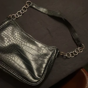 Svart axelväska med kedjedetaljer och besch ny handväska  - Två snygga väskor till salu! Den första är en svart axelväska i skinn med coola kedjedetaljer. Den andra är en beache axelväska i syntet med en elegant design. Perfekta för både vardag och fest!