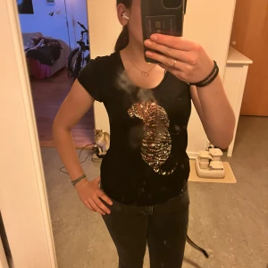 Svart t-shirt med paljettdetalj - Säljer en svart t-shirt i mycket bra skick med en glittrig paljettkatt på framsidan. Perfekt för att piffa upp vardagslooken eller för en festlig kväll. T-shirten är kortärmad och har en normal passform. Superfin och bekväm!