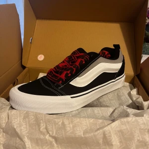 Svart och vit Vans sneaker - Säljer ett par snygga Vans sneakers i svart och vitt med coola röda snören. Skorna är i nytt skick och kommer i originalkartong. Perfekta för både vardag och fest! 🖤